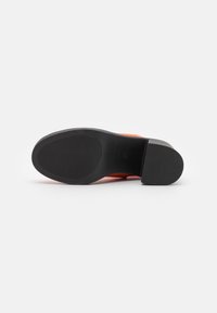Suela de goma negra con agarre texturizado, con una parte superior naranja que es suave y estilizada, diseño cónico, sin herrajes visibles.