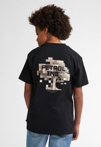 Zwart katoenen T-shirt met een gepixeld boom ontwerp en de tekst "PETROL IND" op de achterkant. Korte mouwen, normale pasvorm, minimalistisch ontwerp.