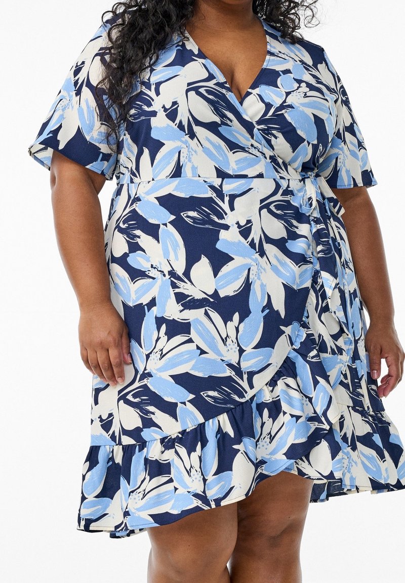 Námořnická modrá zavinovací šaty s květinovým printem v světle modré a bílé. Mají krátké rukávy, volánkový lem a zavázaný pás pro nastavitelný střih.