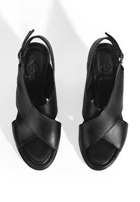 Zwarte leren sandalen met een kruislings ontwerp. Open teen en hiel, met een slingback band voor een veilige pasvorm. Gladde textuur.