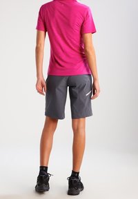 Rosa atletisk kortärmad tröja med en texturerad yta, kombinerad med grå shorts med vit accent och svarta löparskor.