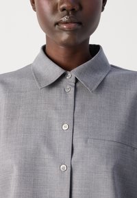 Gray button-up shirt with a collar, featuring a textured fabric, front pocket, and two buttons at the collar.