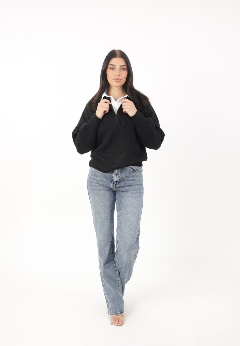 Svart strukturerad tröja med v-ringning, kombinerad med ljusblå högmidjade jeans och klara öppna klackar. Enkel vit skjorta med krage synlig.