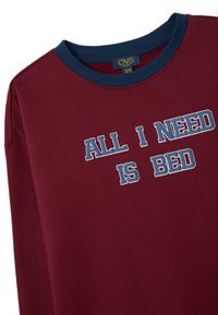 Camiseta de manga larga burdeos con un cuello de canalé azul. Presenta la frase impresa "TODO LO QUE NECESITO ES CAMA" en texto blanco y azul. Tejido suave.