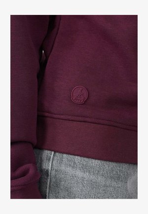 Bordeauxrode sweatshirt met ribgebreide manchetten en onderkant, voorzien van een klein, reliëf logo in een bijpassende tint. Draagt bij grijze denim broek.