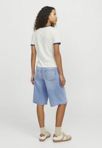 Witte t-shirt met korte mouwen en marineblauwe bies, gecombineerd met lichtblauwe denim shorts, voorzien van twee achterzakken. Draag het met beige crew sokken en sneakers.
