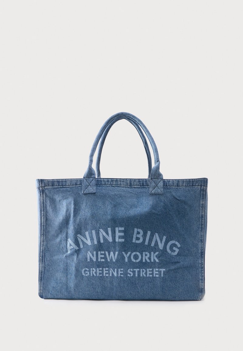 Denim tas met dubbele handvatten met "ANINE BING NEW YORK GREENE STREET" in lichtblauw gedrukt op de voorkant.