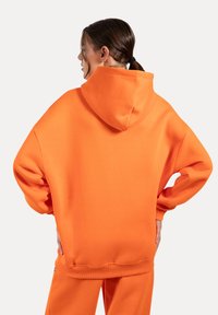 Oversized orange hoodie med en stor hætte, ribbede manchetter og en glat fleece tekstur. Simpelt design, fuld dækning og en levende farve.