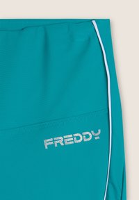 Pantalones cortos deportivos en color turquesa con ribete blanco y el logo "FREDDY" en plata. Fabricados con un material suave y elástico con un diseño ajustado.
