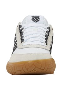 Sneaker blanche avec des rayures noires et des accents en daim gris, dotée d'une semelle en caoutchouc texturé et de lacets blancs, conçue avec un logo sur la languette.