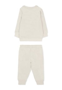 Jasno beżowy zestaw składający się z bluzki z długim rękawem i spodni dresowych. Miękka tkanina, mankiety na rękawach oraz elastyczny pas.