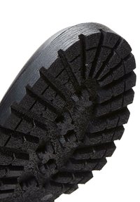 Suela de goma negra con un patrón de banda de rodadura profundo, que presenta prominentes crestas y surcos para la tracción y la estabilidad, superficie texturizada para mejor agarre.