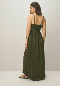 Robe maxi de couleur vert foncé, avec un corsage smocké, des bretelles fines et ajustables, et une jupe fluide. Présente un tissu doux et texturé avec un minimalisme dans les détails.