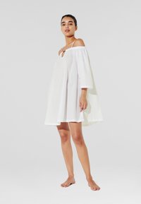 Witte off-shoulder jurk met een sleutelgatdetail en driekwartmouwen. Gemaakt van lichtgewicht stof, met een losse, vloeiende snit.