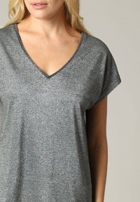 Korte mouwen V-hals top van glinsterende grijze stof, met een ontspannen pasvorm en matte zwarte naadaccenten. Soepele textuur met subtiele glans.