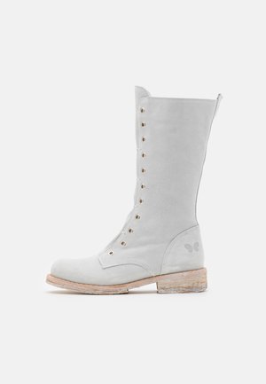 Botte haute en daim gris clair à lacets avec semelle en bois et logo papillon décoratif près du talon, vue de côté sur fond blanc.