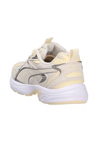 Light beige sneakers with silver accents, textured panels, and a cushioned white sole. Features a yellow heel tab and a lacing system.
