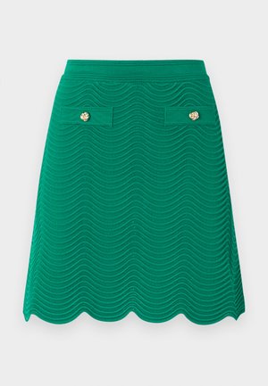 Jupe verte en maille de coupe trapèze avec motif ondulé, ourlet festonné et deux poches à rabat avant ornées de boutons décoratifs dorés.