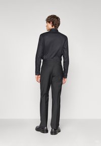 Chemise noire à manches longues associée à un pantalon noir ajusté. La chemise présente un col classique et une texture lisse ; le pantalon a une coupe ajustée.