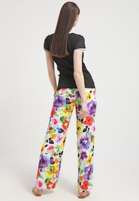 Woman standing with back facing camera wearing black short-sleeve top and wide-leg pants with colorful floral print and open-toe sandals.