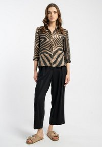 Beżowa i czarna bluzka w paski z zapięciem na guziki z przodu i podwiniętymi rękawami, zestawiona z luźnymi czarnymi spodniami i teksturowanymi beżowymi sandałami.