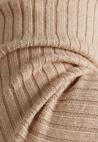 Béžová pletená tkanina s vodorovnou žebrovanou strukturou. Obsahuje jemné variace v tloušťce příze a měkký, mírně fuzzy povrch.