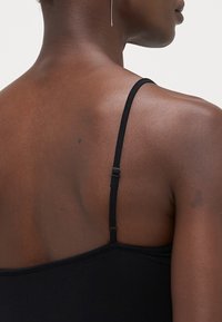 Svart topp med tynne justerbare stropper. Baksiden har en glatt tekstur og et enkelt design, som viser en minimalistisk estetikk.