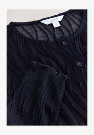 Bluza texturată bleumarin cu pliuri asemănătoare valurilor, cu decolteu rotund și nasturi. Material moale, ușor transparent, cu margini destrămate.