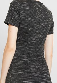Czarna sukienka z krótkimi rękawami, wyróżniająca się teksturowanym, poziomym wzorem w srebrnym kolorze. Materiał ma subtelną połyskliwość i dopasowany krój.