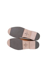 Brązowe skórzane buty z gładką cholewką, jasnobeżową wkładką, gumową podeszwą z teksturowanym gripem oraz nadrukowanym logo marki na spodzie.
