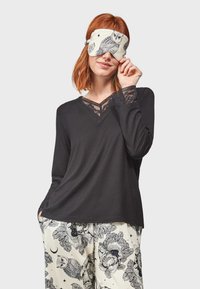 Top noir à manches longues avec des détails en dentelle au niveau de l'encolure et des poignets, associé à un pantalon de pyjama à motifs contenant des fleurs et des hiboux.