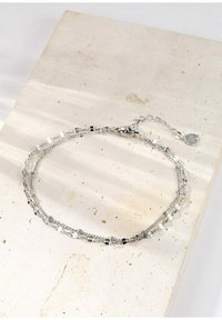 Pulsera de plata con cadenas en capas que presentan eslabones planos y redondos alternados, cierre de mosquetón y un pequeño charm.