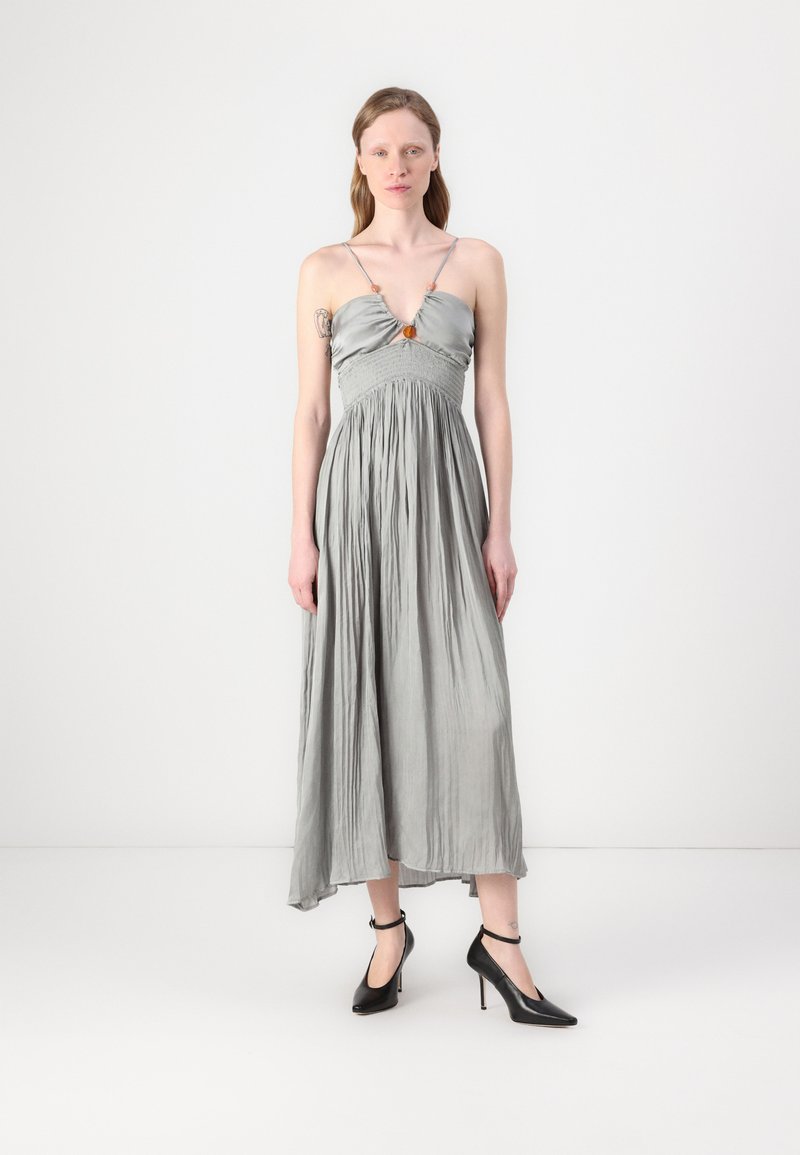 Vestito lungo argento-grigio con corpetto aderente e gonna fluente, caratterizzato da sottili spalline e una vita strutturata. Scarpe nere con tacco alto completano il look.
