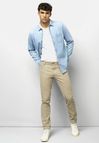 Light blue denim shirt over a white t-shirt, paired with beige slim-fit pants and white sneakers. The shirt features a chest pocket.