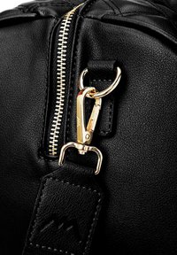 Eck eines schwarzen Lederbeutels mit einem goldenen Reißverschluss, goldenen Beschlägen und einer strukturierten Oberfläche mit Stichdetails am Tragegurt.
