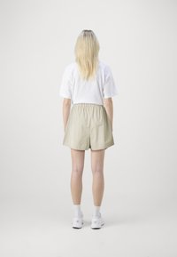 Pantaloni corti leggeri beige con vita elasticizzata, abbinati a una t-shirt bianca a maniche corte, indossati con sneakers bianche e calzini.