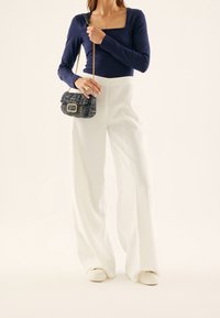 Marinblå långärmad topp med fyrkantig ringning, vita vida byxor och en texturerad svart-vit axelväska med guldfärgade detaljer.