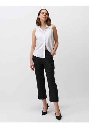 Blusa bianca senza maniche con colletto, abbinata a pantaloni neri cropped con taglio dritto e tasche laterali. Tacchi alti neri completano il look.