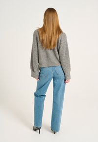 Grauer Strickpullover mit weiten Ärmeln, kombiniert mit hellblauen Jeans im geraden Schnitt. Die Jeans haben Gesäßtaschen und einen hochtaillierten Schnitt.