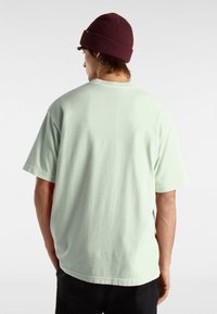 Mintgrünes Baumwoll-T-Shirt mit kurzen Ärmeln, lässiger Passform und rundem Halsausschnitt, kombiniert mit einer tief burgunderfarbenen gerippten Mütze.