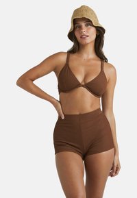 Brauner gerippter Bikini-Oberteil mit verstellbaren Trägern und passenden hochgeschnittenen Shorts, kombiniert mit einem gewebten beigen Bucket Hat.