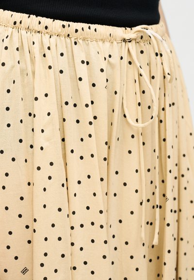 Μπεζ φούστα με μαύρες πουά βούλες, με ελαστική μέση και κορδόνι δεμένο, φορεμένη με μαύρο τοπ.