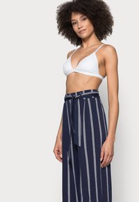 Witte, driehoekige bralette gecombineerd met hoog-taille navybroek met verticale witte strepen en een gestrikte tailleband, zachte stoftextuur.