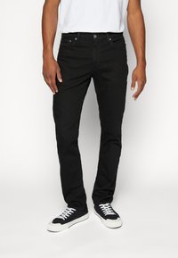 Černé džíny z denimu se slim fit střihem, pěti kapsami, standartním pasem a jemnými detaily šití, doplněné bílou a černou obuví.