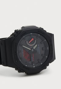 Montre G-Shock noire avec un affichage numérique et analogique, fonction solar tough et bracelet en caoutchouc. Accents rouges notables sur le cadran.
