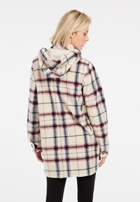 Geruite capuchonjas in beige, roze en zwart. Zachte, gestructureerde stof. Oversized pasvorm met lange mouwen en een relaxte silhoutte.