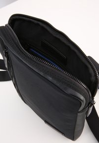 Borsa a tracolla nera con scomparto principale a zip aperta che mostra una tasca interna con zip e una tracolla regolabile.