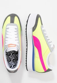 Neon žluté tenisky s růžovými a šedými detaily, bílé tkaničky, texturovaná černá podrážka a vzorovaná černá vložka.