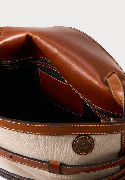 Ανοιχτή μπεζ και καφέ δερμάτινη τσάντα χειρός που δείχνει μαύρη εσωτερική επένδυση, εσωτερική τσέπη με φερμουάρ και καφέ δερμάτινη ετικέτα με το όνομα της μάρκας.