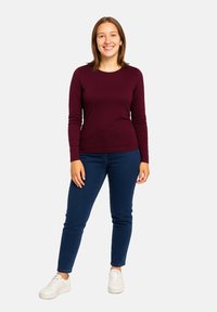 Maglietta bordeaux a maniche lunghe abbinata a jeans blu scuro e sneakers bianche. La maglietta ha un collo rotondo e un design aderente.